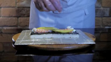 Pirinç dürümleri, suşi pişirme. İçinde pirinç, nori, mango ve karides var. Lezzetli yemek. Aşçı eldiven takıyor.. 