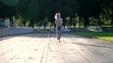 Uzun saçlı çekici kız stadyumda koşuyor. Mavi bluz ve dar tayt giyiyor..