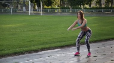 Uzun saçlı çekici kız spor stadyumunda geriniyor. Mavi bir bluz ve dar taytlar giyiyor..