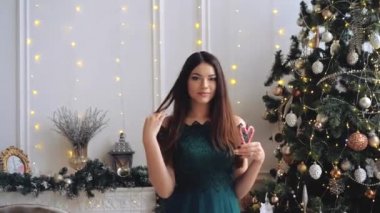 Çekici çekici bir kadın bir eliyle öpücük üflerken diğer eliyle de kalp şeklinde şeker kamışları tutuyor. Büyüleyici bayan gülümsüyor ve Noel süslemeleri önünde eğleniyor.. 