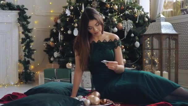 Elegant Långhårig Kvinna Grön Galaklänning Sitter Framför Julgranen Och Tittar — Stockvideo