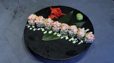 İştah açıcı suşi maki gri arka plandaki siyah tabakta döner. Japon yemek menüsü sunumu. Pirinç ruloları krem peynir ve tobiko kaplıdır.. 