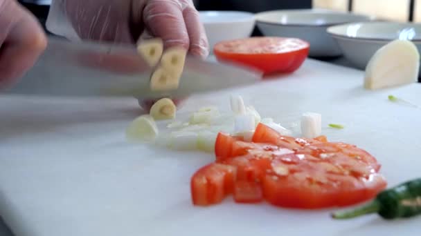 Chef en guantes corta ajo, tomates y jalapeños en la tabla de cortar blanca . — Vídeos de Stock