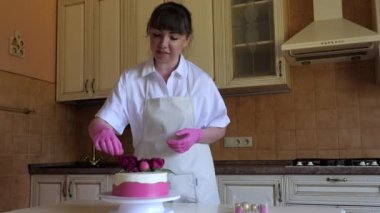 Pembe eldivenli ve beyaz önlüklü pasta şefi kız tatlı pembe bir pasta süslüyor. Sabah kadınları mutfakta..