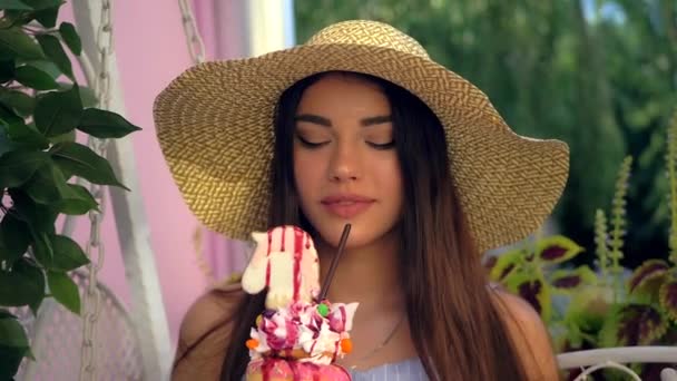 Femme en chapeau à large bord boit milkshake doux, dessert multicouche. — Video