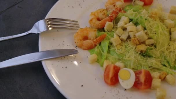 Zblízka pohled na Caesar salát s krevetami podávané na bílém talíři. Nůž a vidlička na talíři. — Stock video