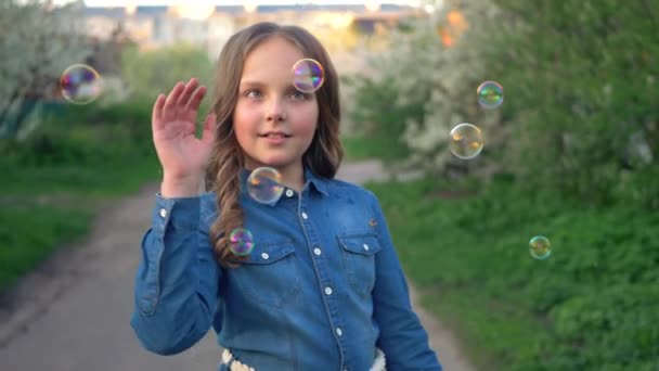 Petite fille dans une robe de soleil en denim bleu attrape de grandes bulles en plein air. — Video