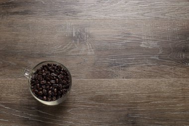 Ahşap bir masaya boşaltmak veya metin için düzenlenmiş koyu kavrulmuş kahve çekirdekleri fincan