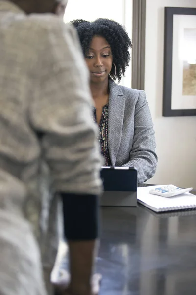 Black female client is upset at tax preparer or CPA accountant in an office.  The image can also depict a manager angry at a secretary.