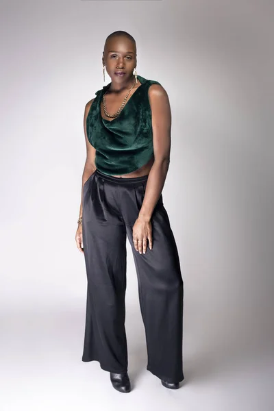 Black African American female fashion model posing with trendy bald hairstyle and stylish clothing in a studio.  She is looking confident and showing beautiful individuality.