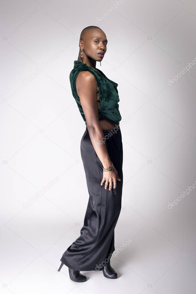 Black African American female fashion model posing with trendy bald hairstyle and stylish clothing in a studio.  She is looking confident and showing beautiful individuality.