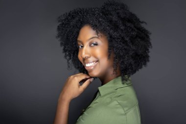 Siyah Afro-Amerikan moda modeli gri bir stüdyo arka plan üzerinde afro saç modeli ile poz. O kendinden emin ve etnik kıvırcık saç kesimi gösteren gülümsüyor.  