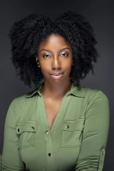 Black African American fashion model posing with afro hairstyle on a gray studio background.  She is confident and smiling showing off the ethnic curly haircut.