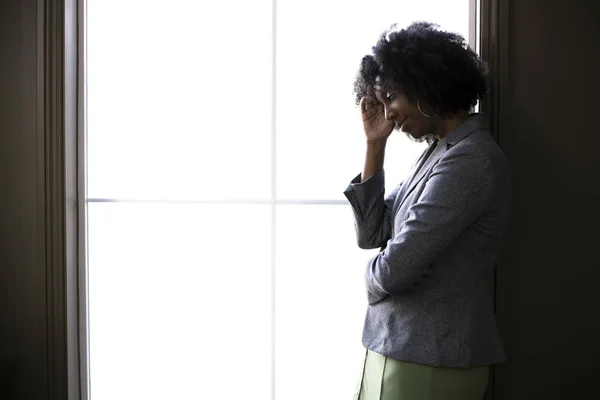 Silhouette of a stressed out black African American businesswoman looking worried and thinking about problems and failure by the office window.  She looks depressed or upset about debt or bankruptcy.