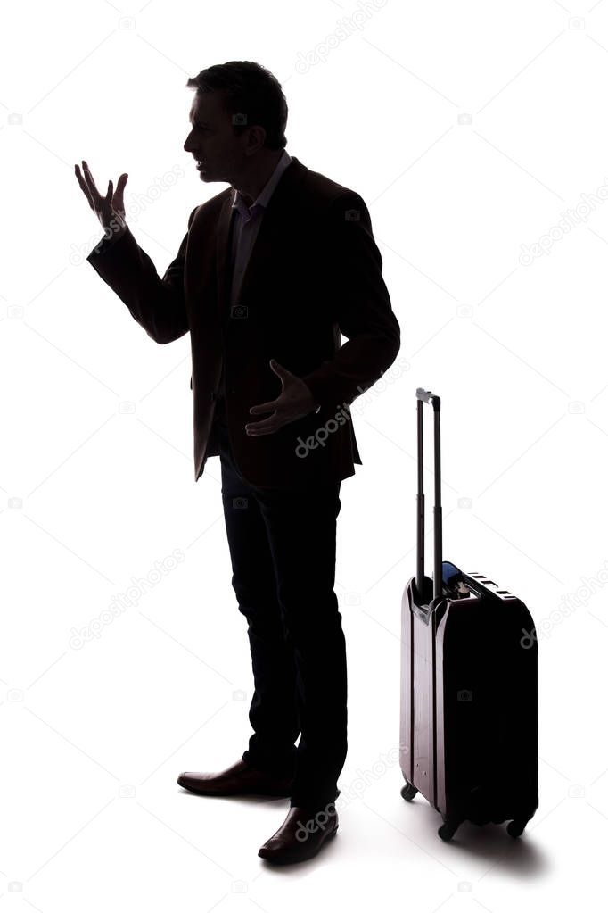 Silhouette of an angry businessman or traveler with luggage as if arguing at an airport about delays or cancellations.  The tourist is angry about the stress of travel. 