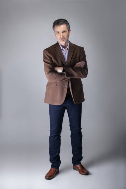 Sakallı orta yaşlı moda modeli olgun ve kendinden emin bir görünüm için iş rahat tarzı kıyafeti ile poz. Moda kahverengi ceket ve kot pantolon ve yüz saç zarif bir giyim gösterir.