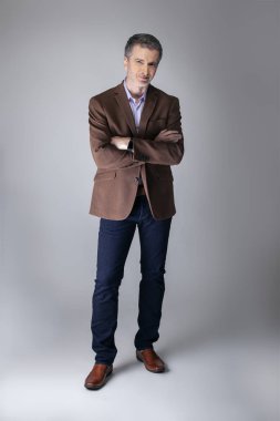 Sakallı orta yaşlı moda modeli olgun ve kendinden emin bir görünüm için iş rahat tarzı kıyafeti ile poz. Moda kahverengi ceket ve kot pantolon ve yüz saç zarif bir giyim gösterir.