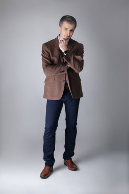 Sakallı orta yaşlı moda modeli olgun ve kendinden emin bir görünüm için iş rahat tarzı kıyafeti ile poz. Moda kahverengi ceket ve kot pantolon ve yüz saç zarif bir giyim gösterir.