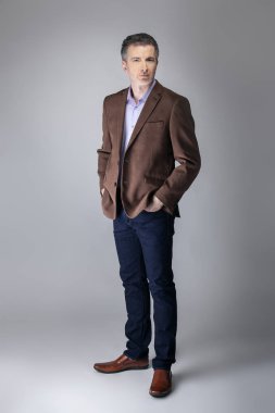 Sakallı orta yaşlı moda modeli olgun ve kendinden emin bir görünüm için iş rahat tarzı kıyafeti ile poz. Moda kahverengi ceket ve kot pantolon ve yüz saç zarif bir giyim gösterir.