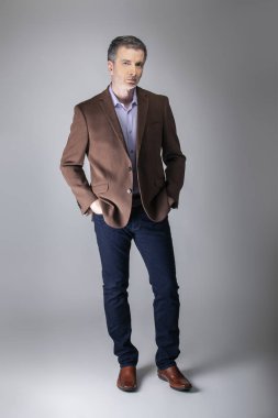Sakallı orta yaşlı moda modeli olgun ve kendinden emin bir görünüm için iş rahat tarzı kıyafeti ile poz. Moda kahverengi ceket ve kot pantolon ve yüz saç zarif bir giyim gösterir.