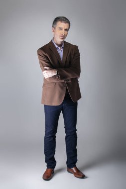 Sakallı orta yaşlı moda modeli olgun ve kendinden emin bir görünüm için iş rahat tarzı kıyafeti ile poz. Moda kahverengi ceket ve kot pantolon ve yüz saç zarif bir giyim gösterir.