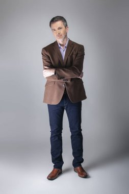 Sakallı orta yaşlı moda modeli olgun ve kendinden emin bir görünüm için iş rahat tarzı kıyafeti ile poz. Moda kahverengi ceket ve kot pantolon ve yüz saç zarif bir giyim gösterir.