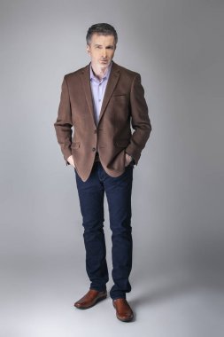 Sakallı orta yaşlı moda modeli olgun ve kendinden emin bir görünüm için iş rahat tarzı kıyafeti ile poz. Moda kahverengi ceket ve kot pantolon ve yüz saç zarif bir giyim gösterir.