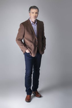 Sakallı orta yaşlı moda modeli olgun ve kendinden emin bir görünüm için iş rahat tarzı kıyafeti ile poz. Moda kahverengi ceket ve kot pantolon ve yüz saç zarif bir giyim gösterir.