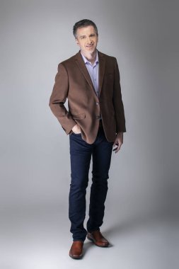 Sakallı orta yaşlı moda modeli olgun ve kendinden emin bir görünüm için iş rahat tarzı kıyafeti ile poz. Moda kahverengi ceket ve kot pantolon ve yüz saç zarif bir giyim gösterir.