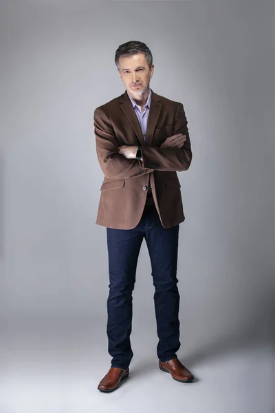 Bearded middle aged fashion model posing with business casual style outfit for mature and confident look.  The trendy brown jacket and jeans and facial hair shows an elegant apparel.
