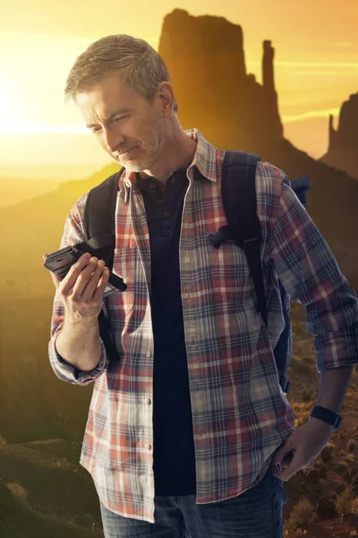 Man hiking in the desert and making a phone call on a cell phone that is able to get network reception.  Being able to use a cell phone is a survival tool for getting help or directions.