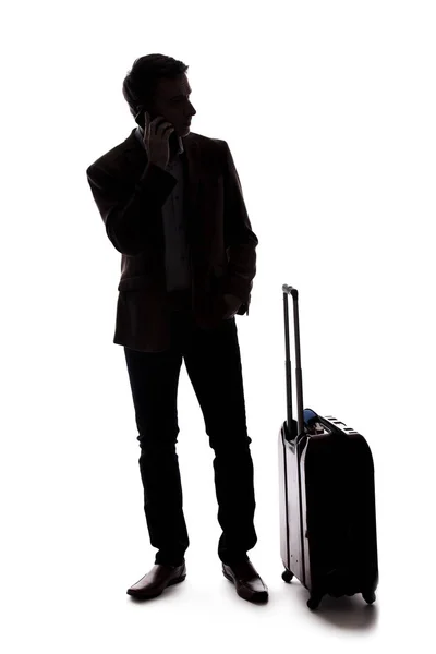 一个商人的剪影 他打电话用手机拼车 他提着行李等着 好像是从机场来的一样 复合材料在白色背景上隔离 — 图库照片