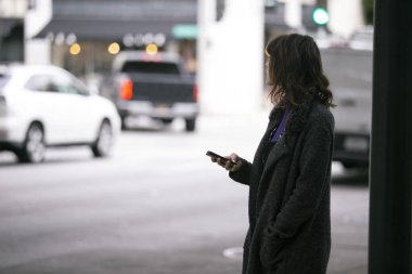 Bir rideshare için kaldırımda bekleyen kadın yaya. Sürücü şehirde onu almak böylece o cep telefonu uygulaması üzerinden onu gps konumunu paylaşıyor. Otomobiller modeli ve plakaları yapmak için bulanık. 