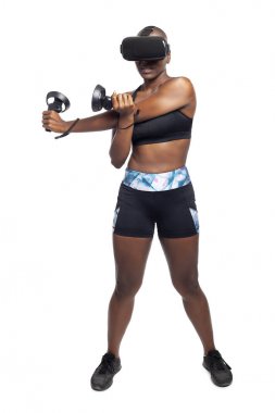 Sanal gerçeklik kulaklık takan ve vr fitness egzersizleri yapan değnek denetleyicileri tutan siyah kadın. Oyun eğlence ve sağlıklı fiziksel aktivite için bir spor simülasyon video oyunu. 
