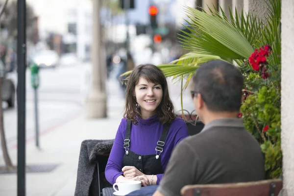 友人やデートのカップルが出会い 都会の歩道カフェでたむろしています 彼らは屋外で社交的に座って コーヒーや朝食を食べみながら話している — ストック写真