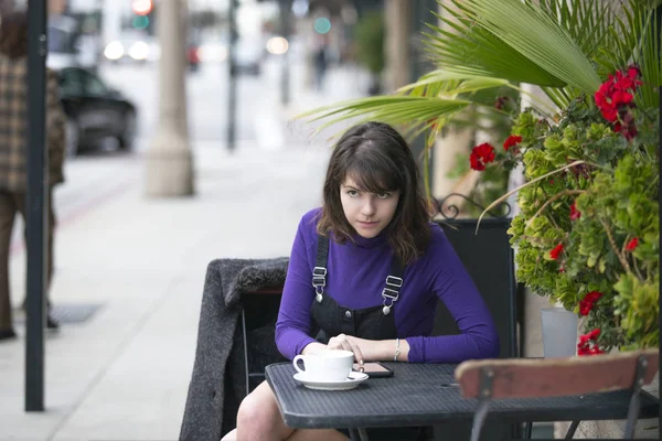 Woman taking a break in an outdoor coffee shop or local cafe in the city and waiting to meet a friend.  She is sitting down in a sidewalk restaurant hanging out. Depicts local business.