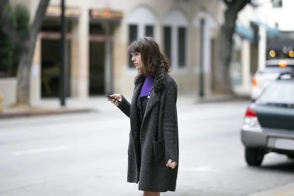 Young female using mobile phone app and waiting for a rideshare or pedestrian tourist checking online map for gps navigation.  Depicts city life and how millennials travel.