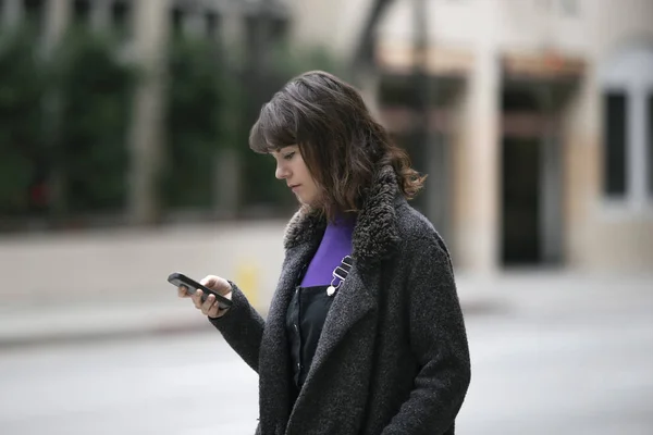 Young female using mobile phone app and waiting for a rideshare or pedestrian tourist checking online map for gps navigation.  Depicts city life and how millennials travel.