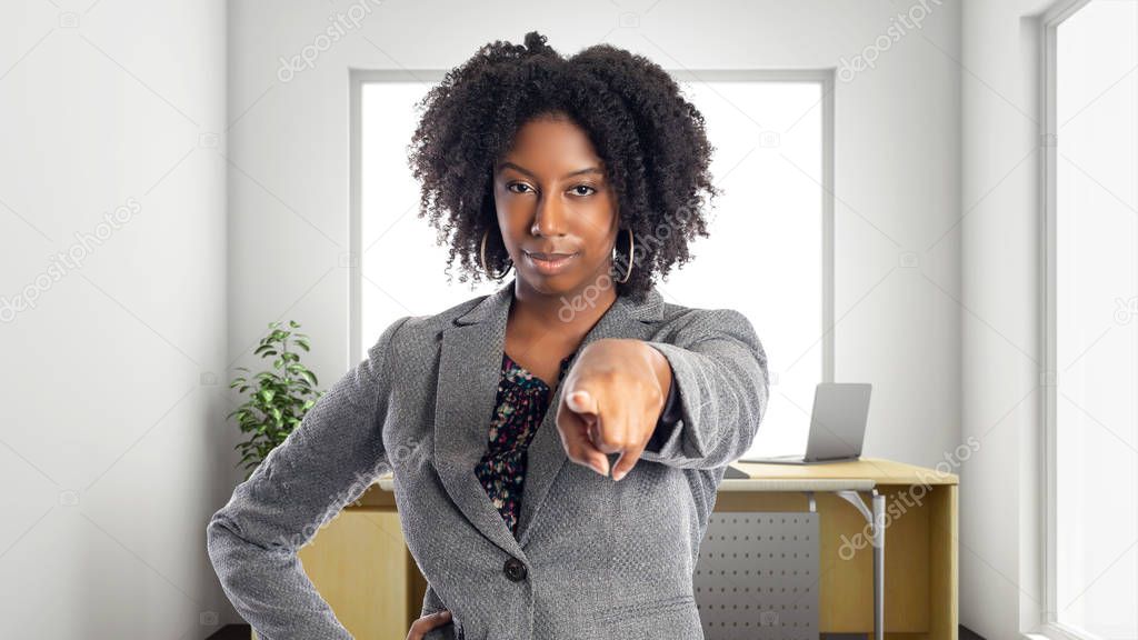 Black African American businesswoman in an office pointing forward.  She is an owner or an executive of the workplace.  Depicts careers and startup business. 