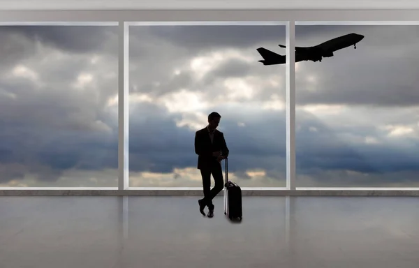 Silhouette of a traveling businessman with luggage in front of an airport window with a view of the sky and an airplane.  The panorama has copy space for text.  Depicts business travel.