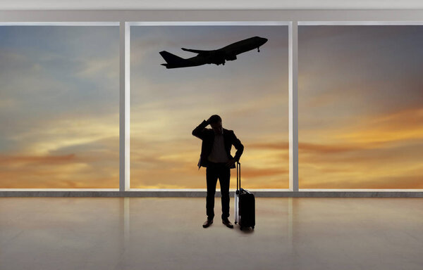 Silhouette of a traveling businessman with luggage in front of an airport window with a view of the sky and an airplane.  The panorama has copy space for text.  Depicts business travel.  