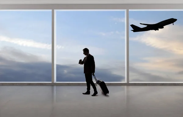 Silhouette of a traveling businessman with luggage in front of an airport window with a view of the sky and an airplane.  The panorama has copy space for text.  Depicts business travel.