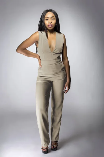 Beautiful black African American fashion model posing with humus grey or khaki clothing in a studio for fall collection catalog.  She is confidently showing the sleeveless top and matching pants.