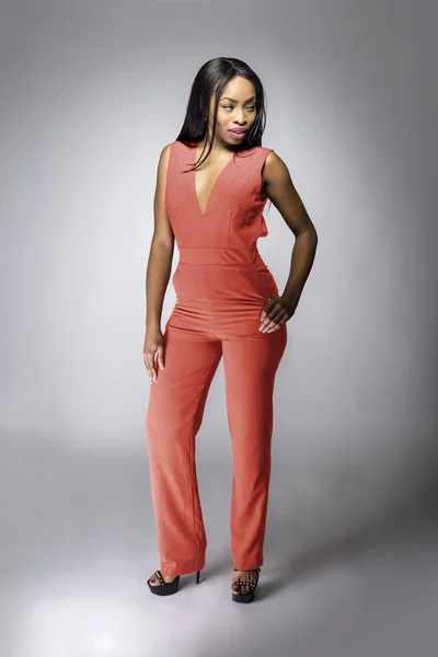 Beautiful black African American fashion model posing with pink or orange clothing in a studio for fall collection catalog.  She is confidently showing the sleeveless top and matching pants.