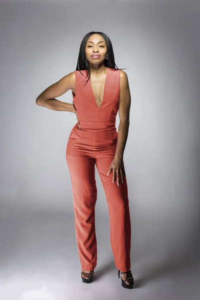 Beautiful black African American fashion model posing with pink or orange clothing in a studio for fall collection catalog.  She is confidently showing the sleeveless top and matching pants.