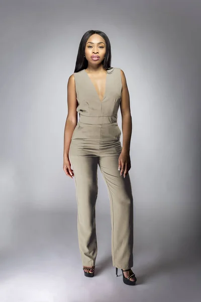 Beautiful black African American fashion model posing with humus grey or khaki clothing in a studio for fall collection catalog.  She is confidently showing the sleeveless top and matching pants.