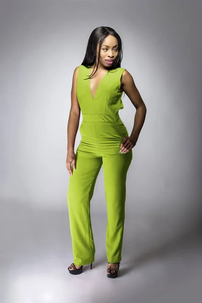 African American fashion model posing with lime green v-neck jumpsuit in a studio for fall collection catalog.  She is confidently showing the sleeveless top and matching pants.