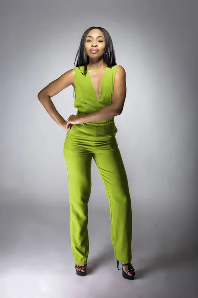 African American fashion model posing with lime green v-neck jumpsuit in a studio for fall collection catalog.  She is confidently showing the sleeveless top and matching pants.