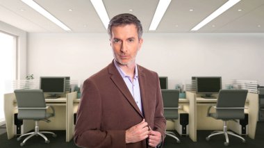 Middle-Aged businessman with gray hair and wearing a brown jacket standing in an office.  Depicts startup and corporate business.  He is looking confident or arrogant.