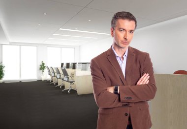 Middle-Aged businessman with gray hair and wearing a brown jacket standing in an office.  Depicts startup and corporate business.  He is looking confident or arrogant.
